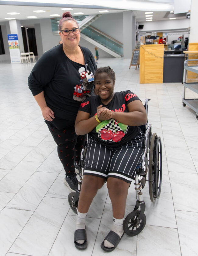 A smiling young guest in a wheelchair with a companion at the Holiday SMILES party