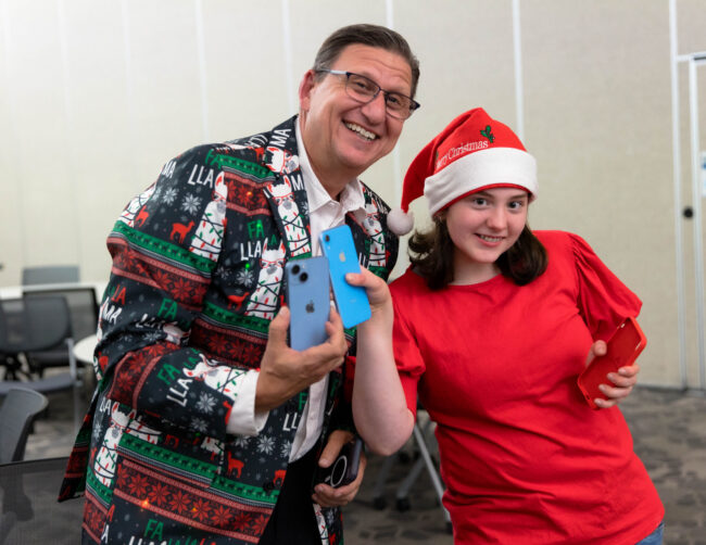 A guest in a Santa hat laughing with a volunteer in a holiday jacket
