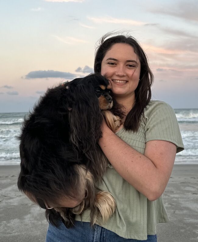 Sarah holding her dog on the beach at sunset